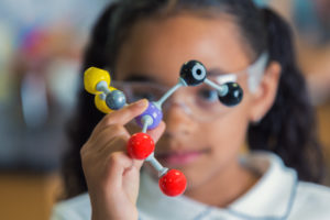 Close up of African American female elementary age student holds a model of the molecular structure. Focus is on the model, the girl is blurred in the background.