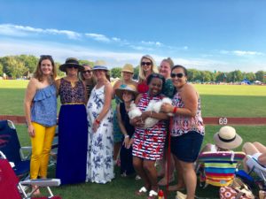 A group of ten JL Boston members at Newport Polo Grounds for Picnic and Ponies event, standing in front of a green field and blue sky