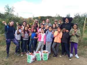 A group of young girls and Junior League volunteers pose in an apple orchard with the apples they have picked