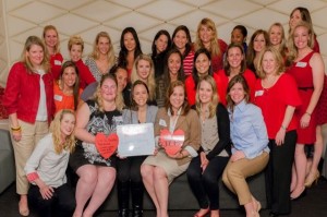 Color image of a group of about twenty women, many of them wearing red, looking at the camera and holding cut-out paper hearts